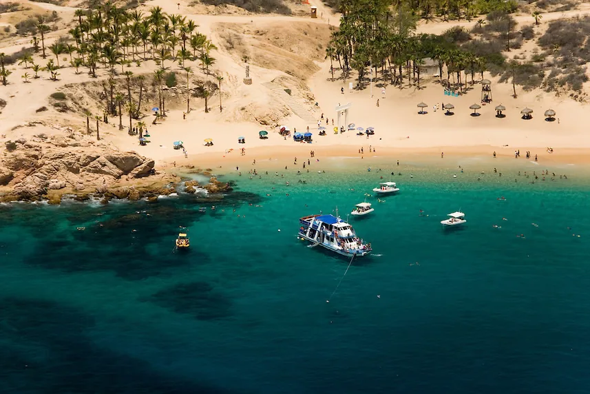Chileno Beach with shade palapas and palm trees above the bay and boats in the water