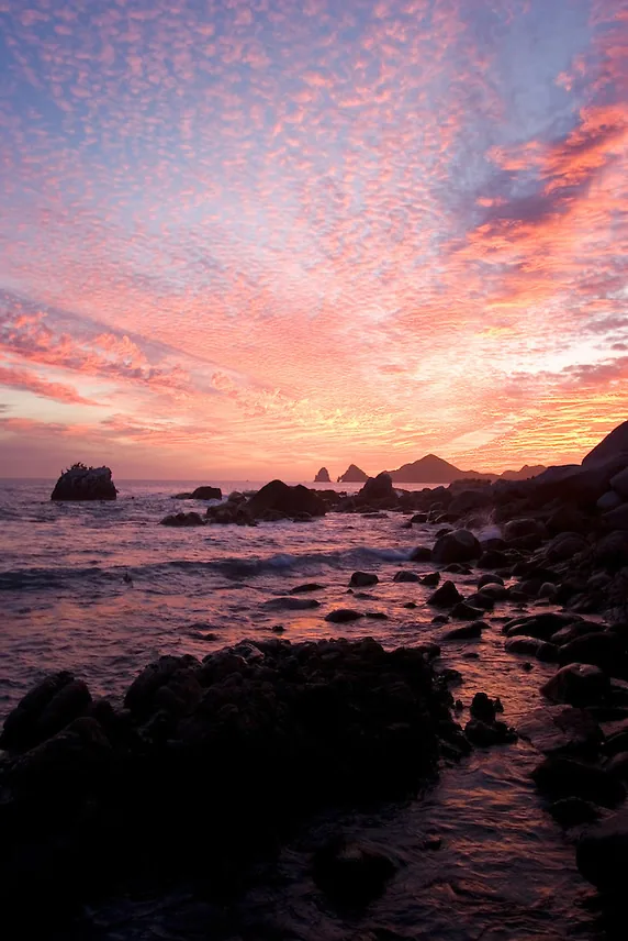Sunset over the rocky shore at Monuments Beach, with Land's End on the horizon