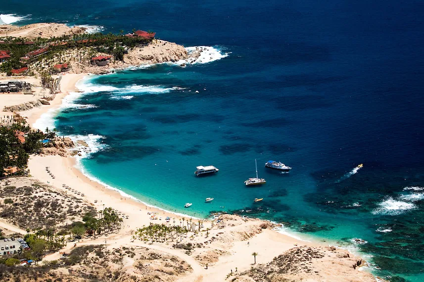 Vista aérea de la caleta de Playa El Chileno, con agua turquesa y lanchas fondeadas frente a la arena, Los Cabos