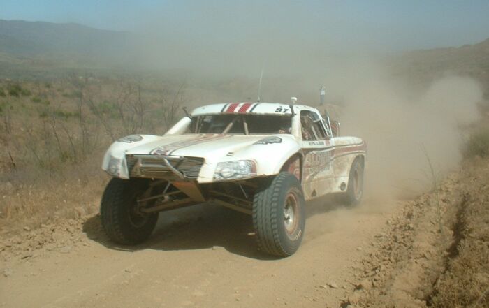 SCORE Trophy Truck racing down a dusty dirt road in Baja California